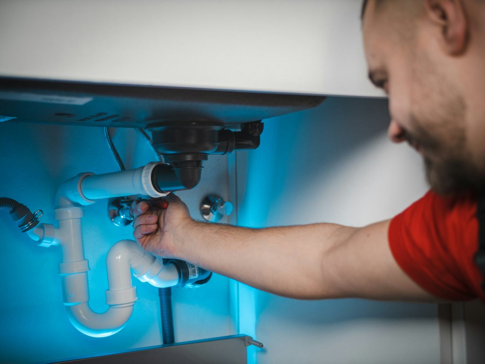 Plumber tightening a drain fitting under a sink