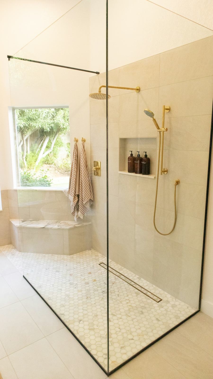 Walk-in glass shower with brass fixtures and a linear drain